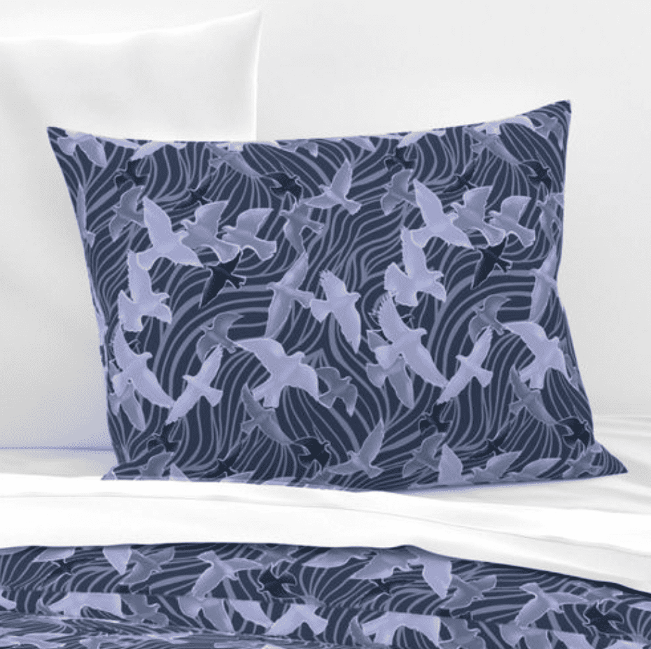 A repeat pattern of a flock of birds flying every which way, outlined in periwinkle, filled with different shades of indigo and purple with glowing highlights on each bird to make out their shape. They are flying over a series of dark blue fluid like curvy stripes that cover the entire background. The pattern is demoed on a rectangular pillow. 