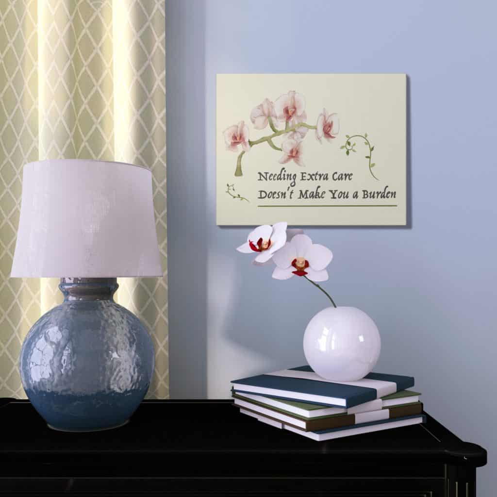 A watercolor illustration of a white, peach, & red orchid with an olive green stem, stretching over the inked words, “Needing extra care doesn’t make you a burden.” The text is framed with thin green vines and a green line underneath. The whole design is demoed on a pale orange canvas mounted on a blue wall next to a real orchid in a pretty white pot. 