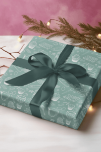 Turquoise wrapping paper with a repeat pattern of baking elements, like cupcakes, pies, cookies, whisks, rolling pins, measuring spoons, sprinkles, flour and sugar outlined in a cartoon style, in white. It is on a present wrapped in dark green ribbon