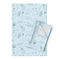 A repeat pattern of baking elements, like cupcakes, pies, cookies, bread, whisks, rolling pins, measuring spoons, eggs, sprinkles, chocolate, flour and sugar drawn in outlines in a cute cartoon style, in bright blue on a pale blue background. The pattern is demoed on a rectangular dishcloth with white stitching.