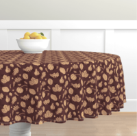 A repeat pattern of fall related elements in orange, drawn with outlines that shift between multiple shades of pink, purple, and maroon. There are several types of leaves, small pumpkins, a squash, pinecones, and acorns. The background is maroon with a series of darker maroon triangles. The pattern is demoed on a round tablecloth that hangs several feet past the edge of the circular table it covers.