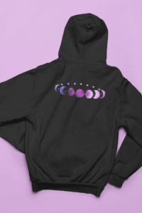7 phases of the moon in a gradient of the genderfluid pride colors: blue, black, purple, white, and pink. It is demoed on the back of a black zip-up hoodie laid flat on a purple background.