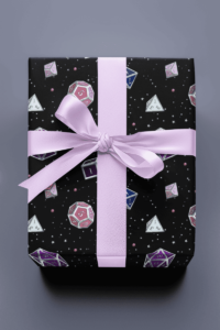 Black wrapping paper with a repeat pattern of 7 Dungeons and Dragons Dice in Genderfluid Pride Flag colors: pink, blue, purple, and white, with tiny white and pink stars in the background. It is on a present with a lavender ribbon and bow.