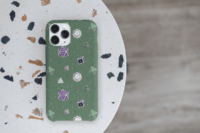 A repeating pattern of 7 Dungeons and Dragons Dice in Genderqueer Pride Flag colors: Purple, white, black, and green on a forest green background. It is demoed on an iPhone 14 Pro Max sitting on a white table.