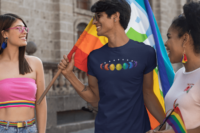 7 phases of the moon in a gradient of 7 colors of the rainbow. It is demoed on a navy T-shirt on a young gay man holding a large rainbow pride flag, with two friends at a pride march.