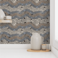A repeat pattern of mosaic tiles in a series of colorful waves. There is a stripe of tan followed by a stripe of grey blue, and then a break of beige, then blue, tan, blue, and beige again. There are darker brown tiles sprinkled through out. The textured grout is medium grey. The pattern is demoed on kitchen wall paper with a beige pitcher and cup sitting on a white counter in front of it.