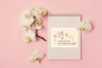 A 4 x 6 inch sticker with a white, peach, and red orchid, and olive green stem, stretching over the inked words, Needing extra care doesnt make you a burden. It is on a pale yellow, watercolor paper textured background on a notebook next to orchids.