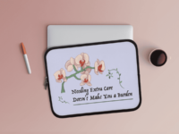 A laptop sleeve with a black zipper and a colorful drawing of a peach and red orchid on a green stem arching over decorative text saying Needing extra care doesnt make you a burden, on a periwinkle background. The words are framed by green vines. The laptop sleeve sits on a mauve flat background, with a silver laptop peeking out of it.
