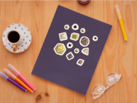 A set of 13 small stickers of the 7 Dungeons and Dragons Dice, as well as orbs and stars, in nonbinary pride colors: yellow, white, black and purple. The stickers have a white border and are displayed on a dark purple notebook.