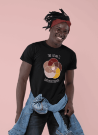 Five interlocking circles of color with white borders arranged in a flower , in shades of pink, maroon, brown, and canary yellow. White text above and below says The Future Is Intersectional. It is on a black T-shirt worn by a happy black man.