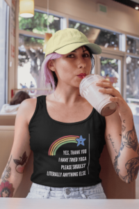 A cartoon of a smiling blue star at the end of a rainbow. Below in all caps white letters it says Yes Thank you I have tried yoga please suggest literally anything else. It is demoed on a black unisex tank top on a woman with pink hair and tattoos.