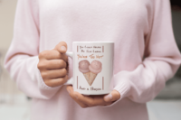 A person in a pink sweater holds a pink mug with a pair of pink and orange ice cream cones covered in sprinkles angled to create a heart. In brown and orange it says You could never be ice cream, you are too hot, and a person.