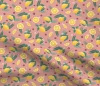 A repeat pattern of lemons, lemon slices, and lemon wedges, interspersed with green leaves, ferns, small red flowers, and small pink flowers. The background is salmon with small pink dots. The pattern is demoed on a piece of rippling fabric.