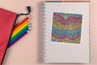 A 4 by 6 inch square sticker with a design of a detailed mosaic of abstract waves in the colors of the pansexual pride flag, hot pink, yellow, and turquuoise. It has a white border and is on a blank notebook next to colored pencils in rainbow order.