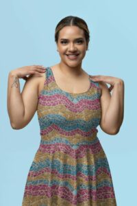 A smiling Latina woman wearing a sleeveless A-line skater dress with a repeat pattern of abstract waves in colors of the pansexual pride flag in a detailed mosaic texture.