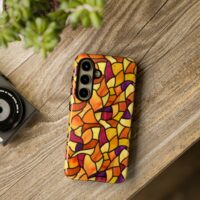 A Samsung Galaxy S24 phone case with a vibrantly colorful repeat pattern of stained glass in abstract flowing shapes in vivid shades of yellow, orange, magenta, and purple. The phone is sitting on a wooden table next to a plant.