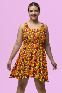 A smiling Latina woman wearing a sleeveless scoop neck skater dress with a vibrantly colorful repeat pattern of stained glass in abstract flowing shapes in vivid shades of yellow, orange, magenta, and purple. There is a light pink background behind her.